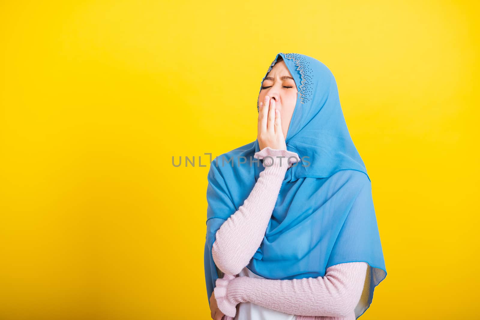 Asian Muslim Arab, Portrait of happy beautiful young woman Islam religious wear veil hijab funny she sleepy yawning wide open mouth hand cover mouth eyes closed studio shot isolated yellow background