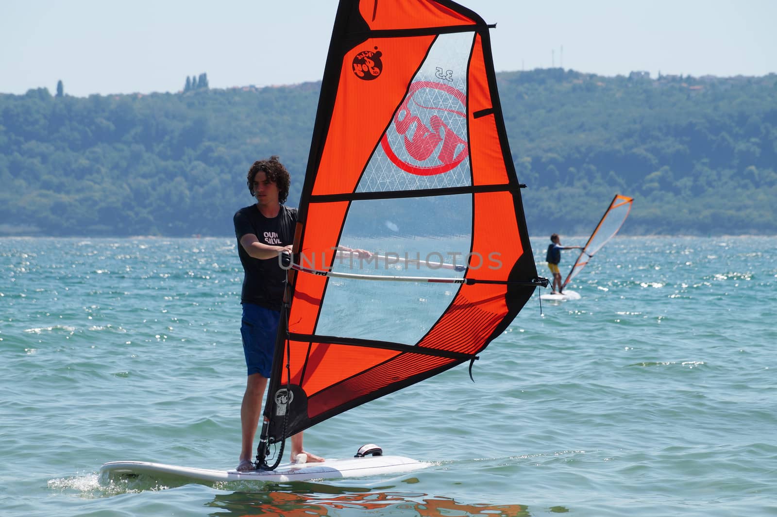 young guy windsurfing in the sea on sunny day by Annado