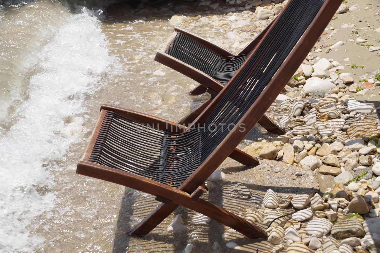 two empty wooden sun loungers on the seashore by Annado