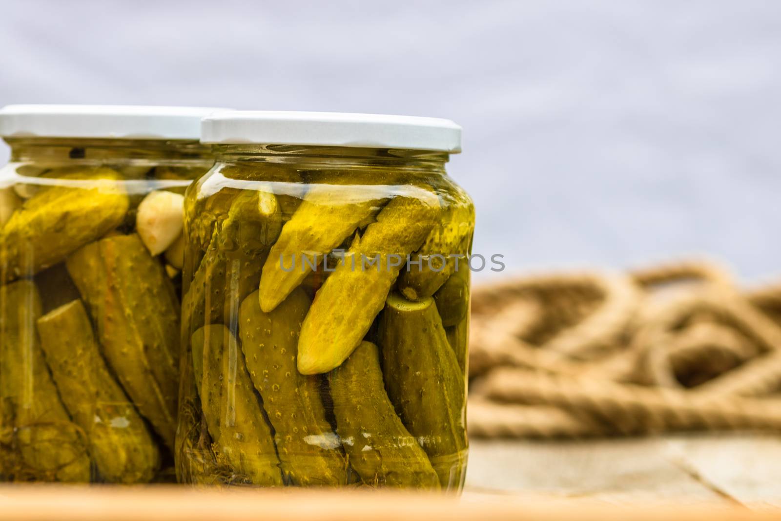 Glass jars with pickled red bell peppers and pickled cucumbers (pickles) isolated. Jars with variety of pickled vegetables. Preserved food concept in a rustic composition.