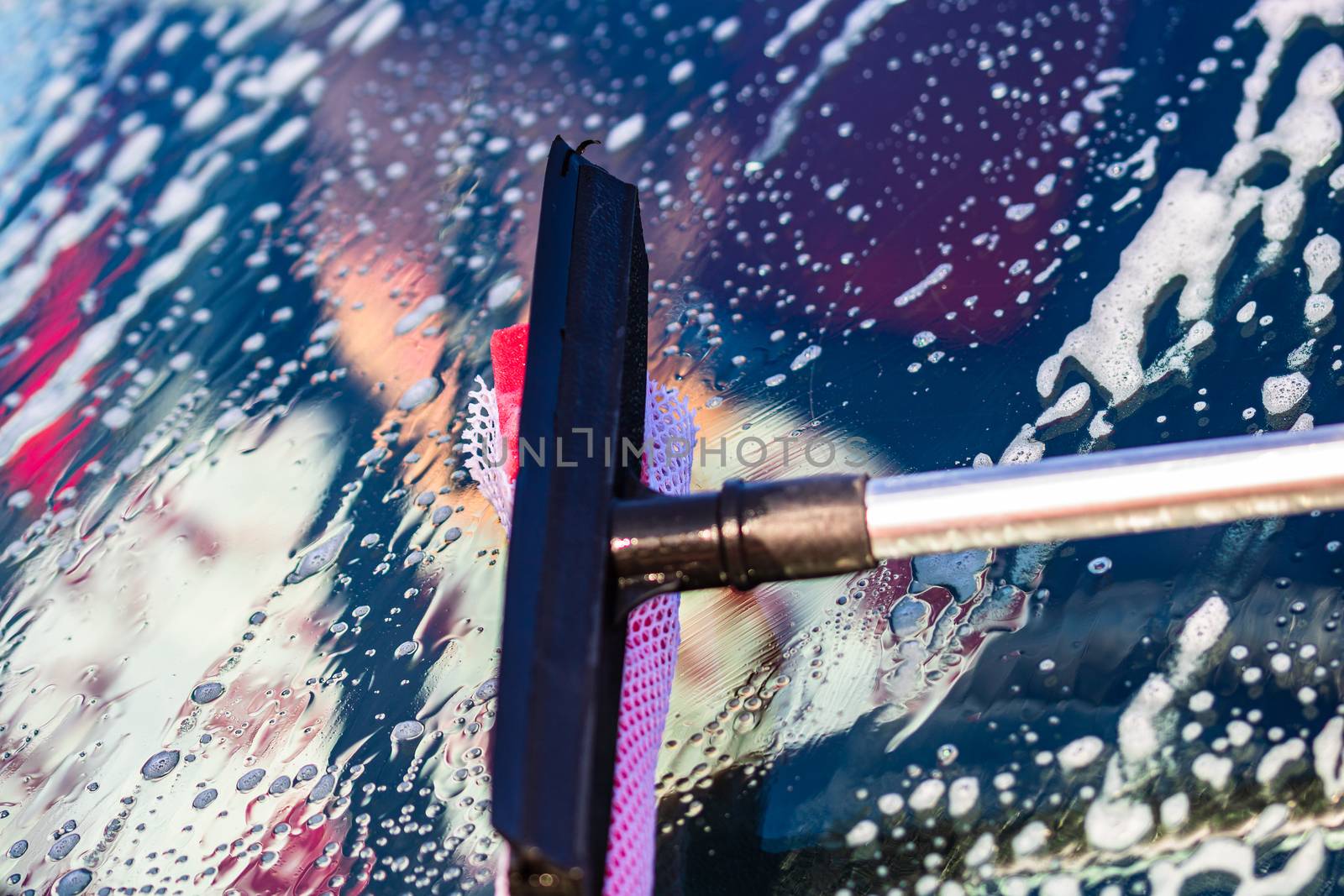 Washing and cleaning the front window of a car with mop in self service car wash station, close up isolated.