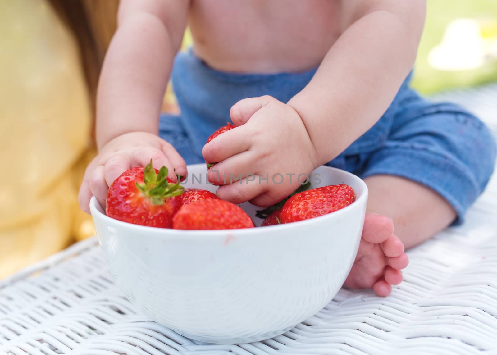 a child grabbing strawberries from a bowl by Iryna_Melnyk