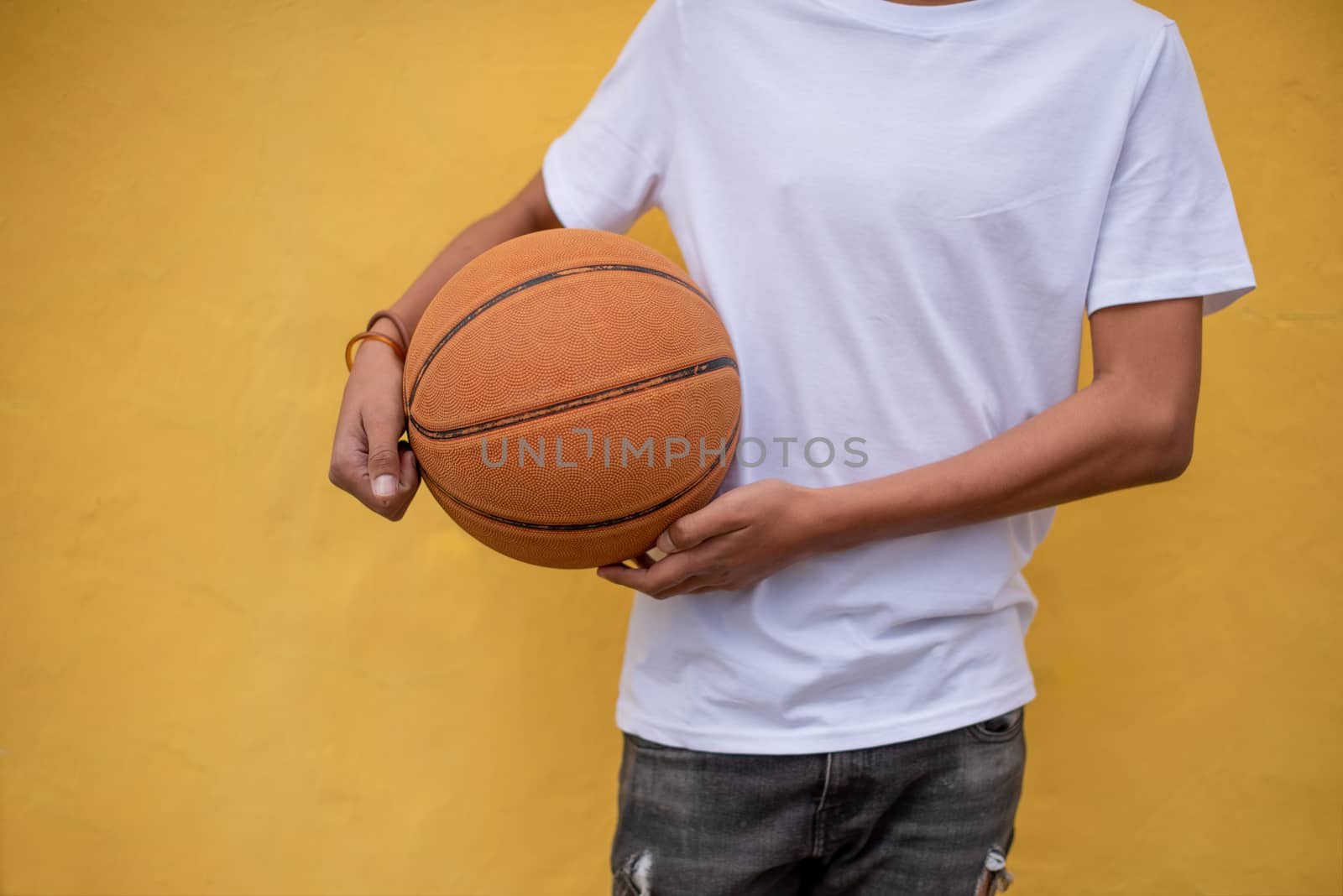 Basketball in hand of young person against yellow background