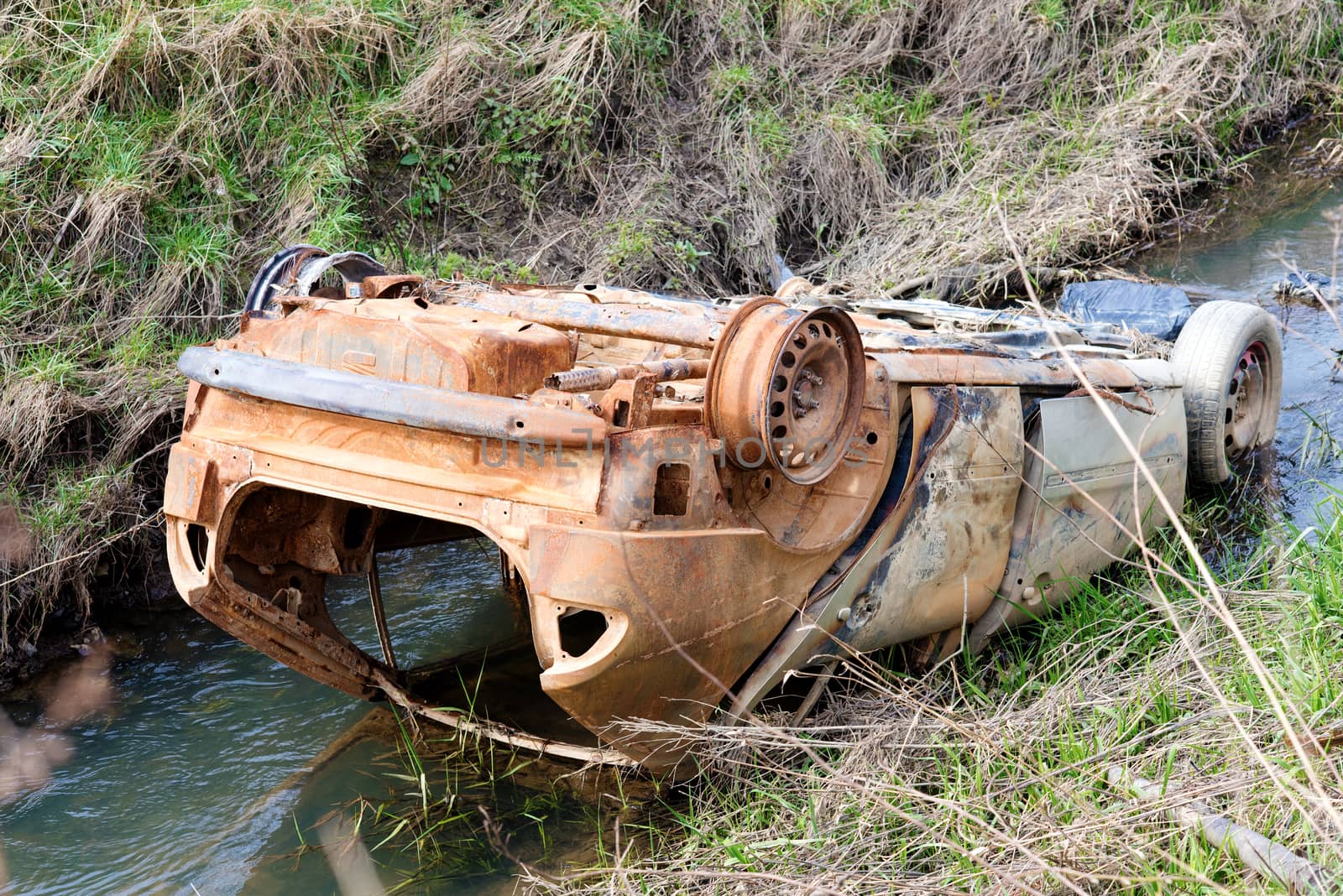 Stolen burnt rusty car abandoned in a river in a countriside polluting the environment