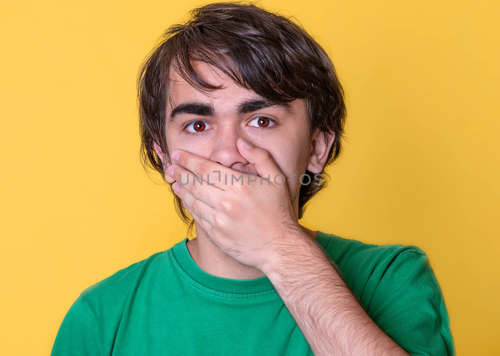 the young man putting his hand over his mouth on yellow background