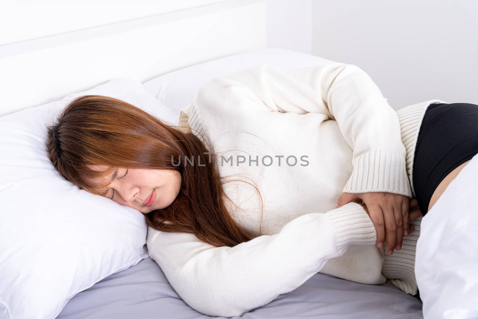 Young woman suffering stomach aches lying on the bed. Healthcare medical or daily life concept.