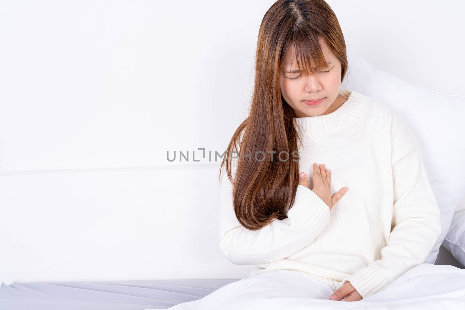 Young woman suffering from chest pain after wake up on the bed. Healthcare medical or daily life concept. by mikesaran