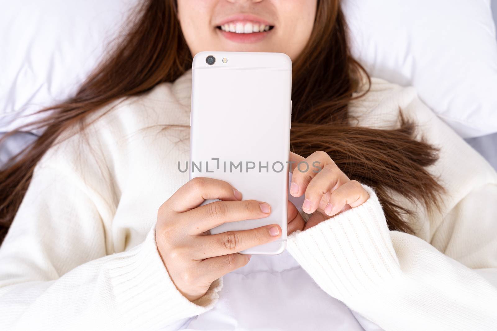Happy Asian girl using a mobile phone lying on the bed at home. Social and technology concept. by mikesaran