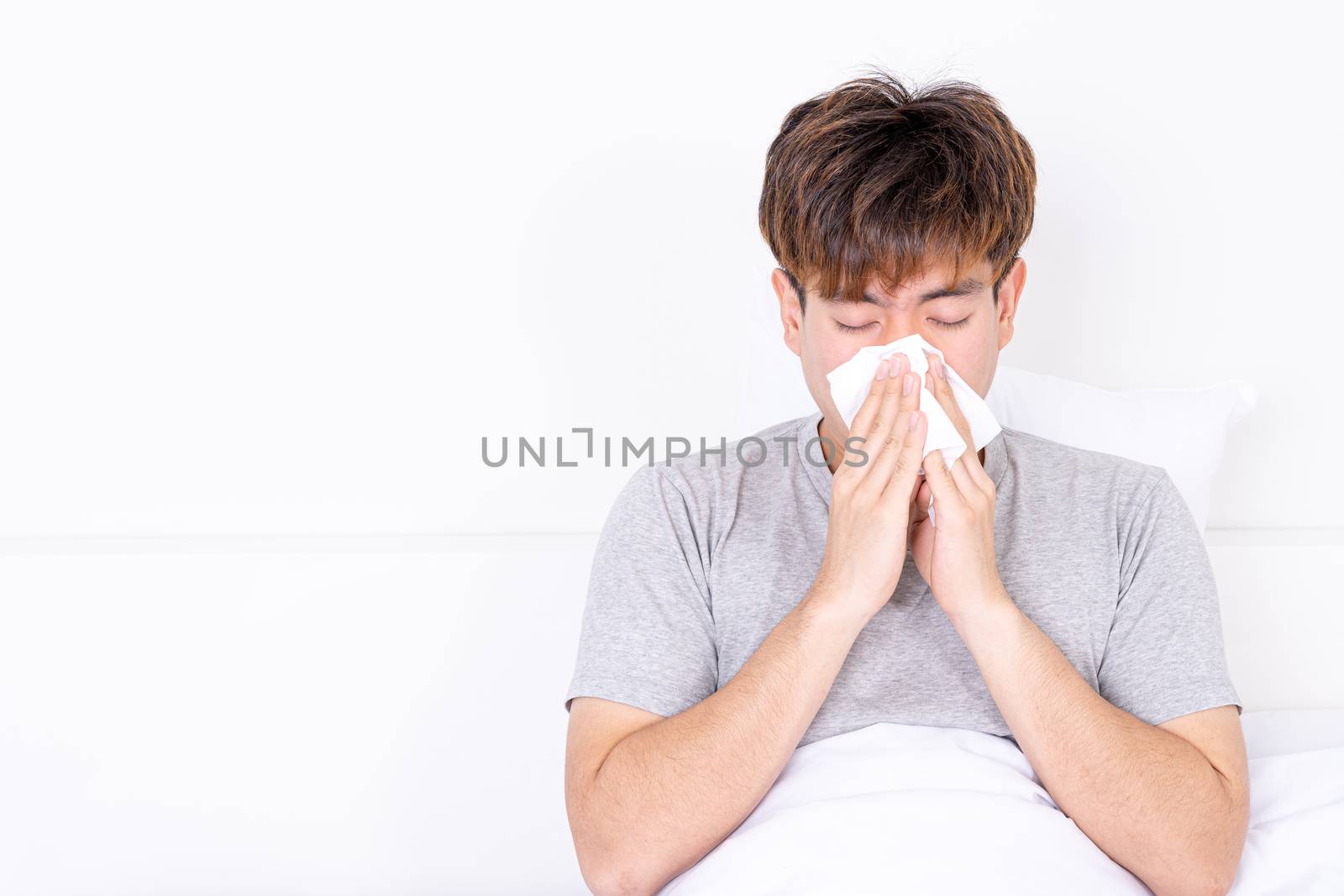 Asian man blowing a nose to tissue lying on the bed at home. Healthcare medical or daily life concept.