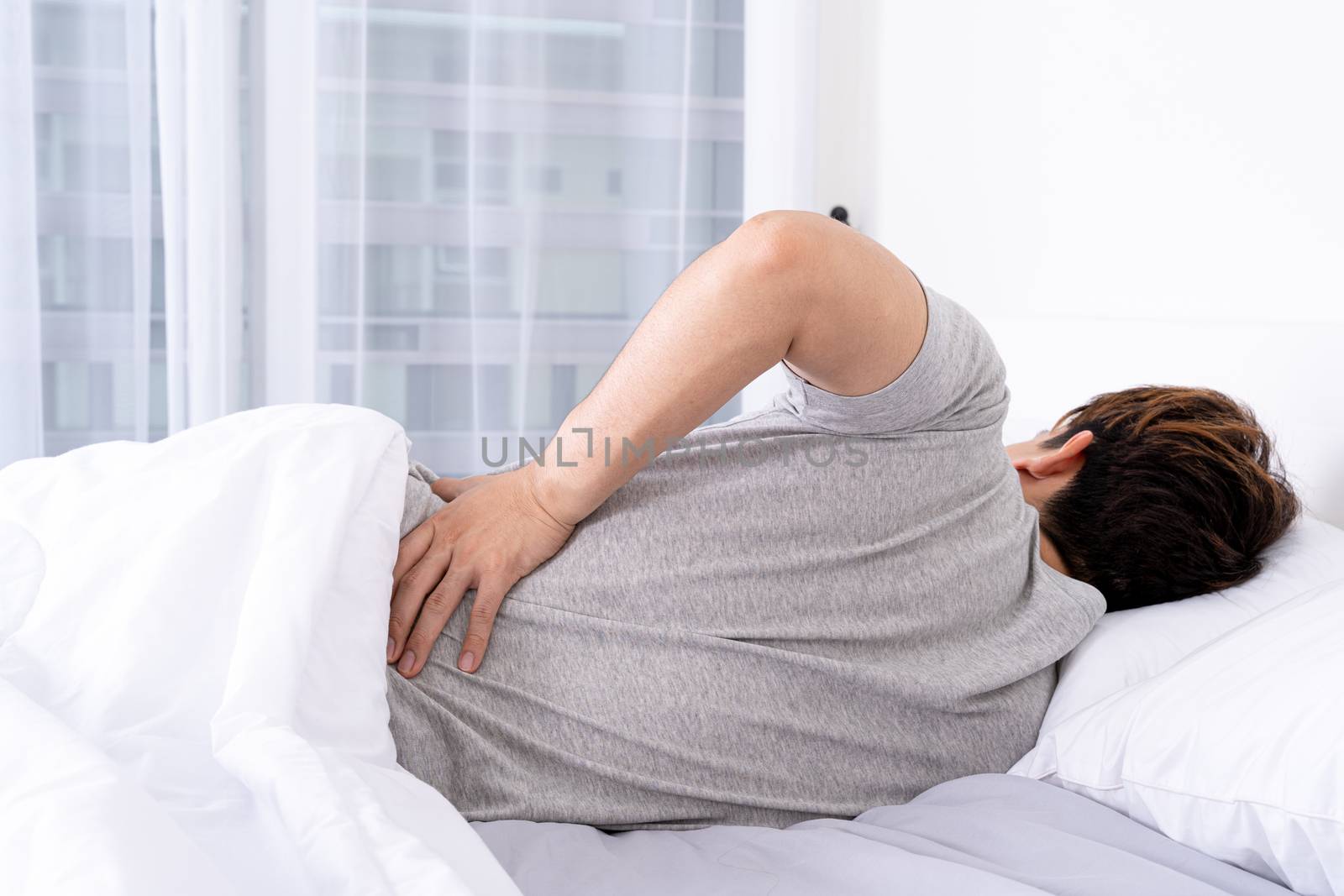 Young man suffering back pain from uncomfortable bed. Healthcare medical or daily life concept.