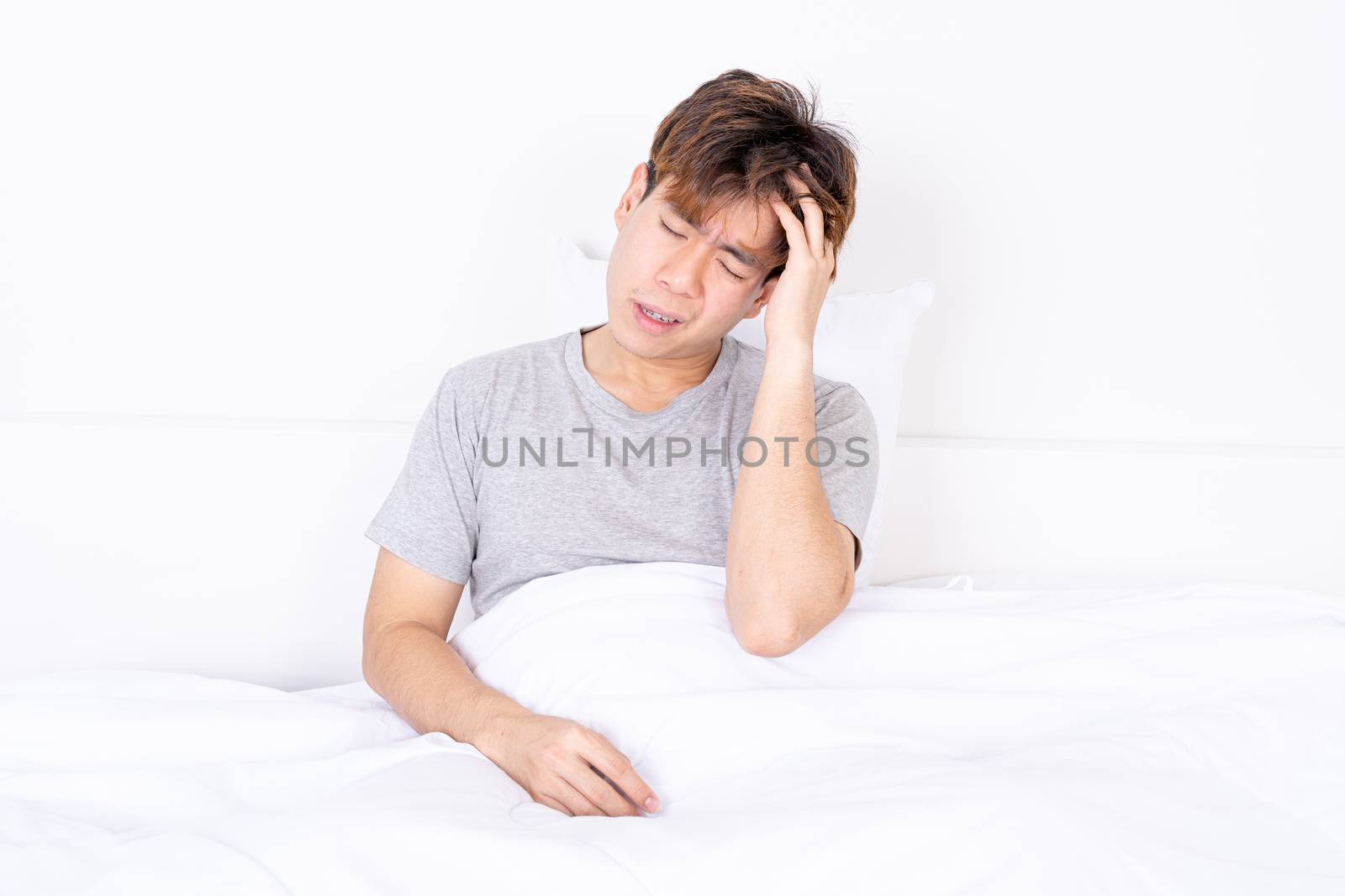 Young man suffering from headaches after wake up on the bed. Healthcare medical or daily life concept.