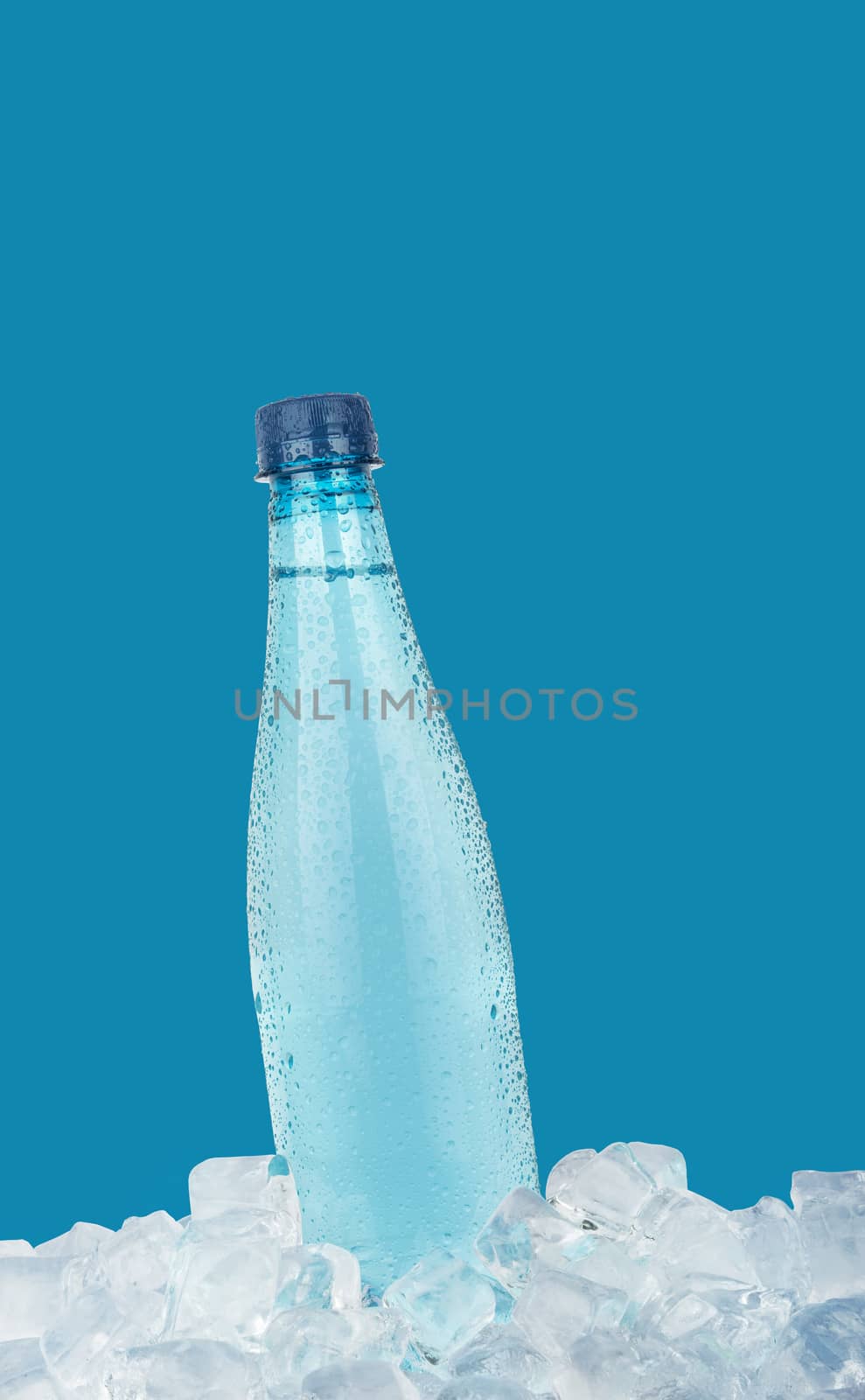One full PET plastic bottle of cold still drinking water chilling on ice cubes isolated on blue background, low angle side view
