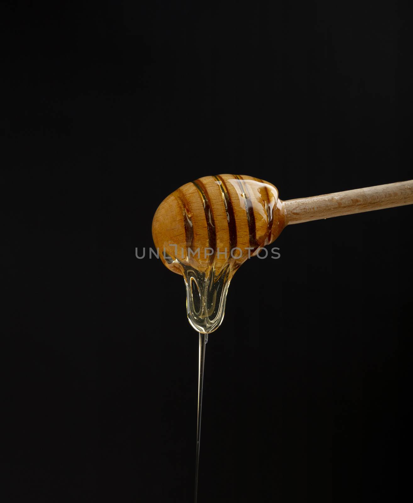 Close up fresh thick fluid acacia honey pouring and flowing from wooden dipper spoon isolated on black background with copy space, low angle side view