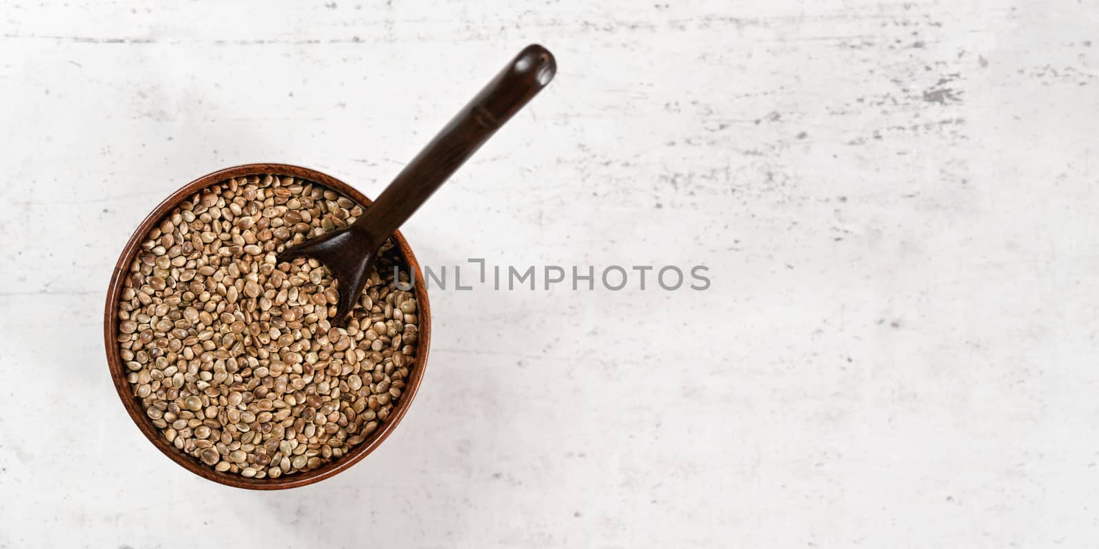 Unpeeled hemp - Cannabis sativa - in small dark wooden cup with spoon view from above, white stone like board space for text under.