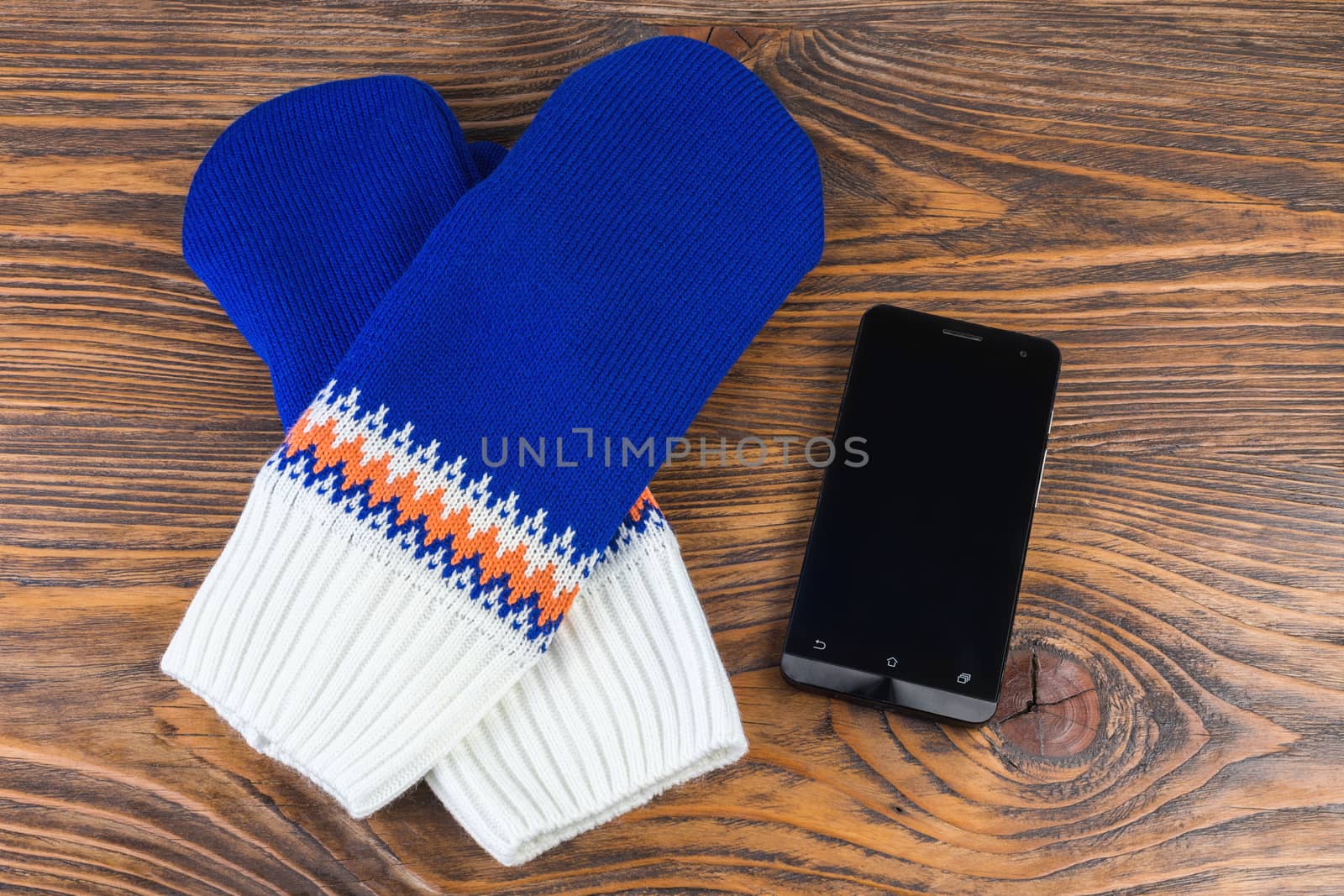 blue and white knited mittens with cellphone on wooden background.