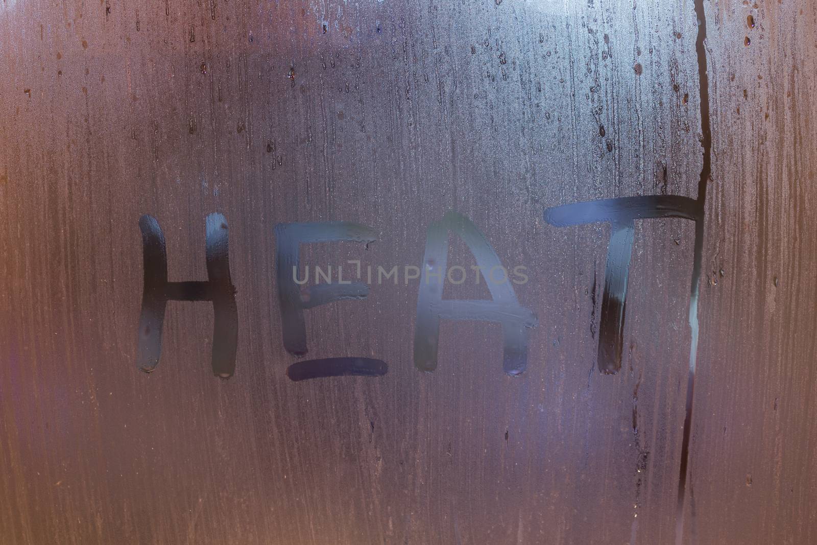 the word heat written on night wet window glass close-up with bokeh background.