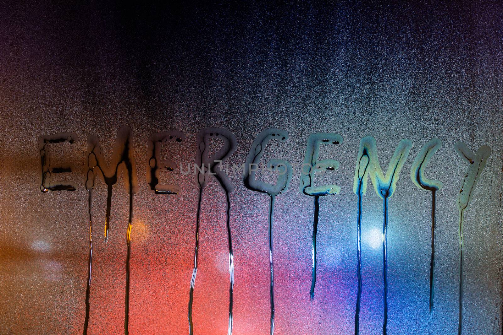 the word emergency written on night wet window glass close-up with blurred background.