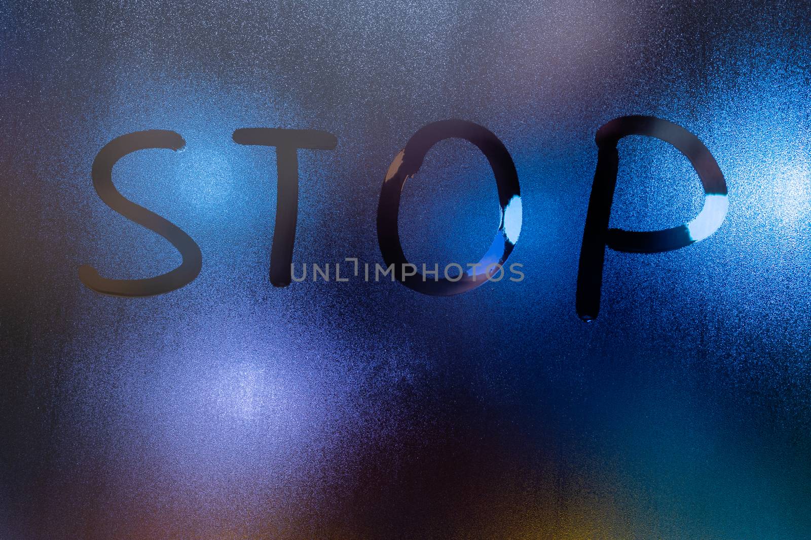 the word stop written on night wet window glass close-up with blurred background.