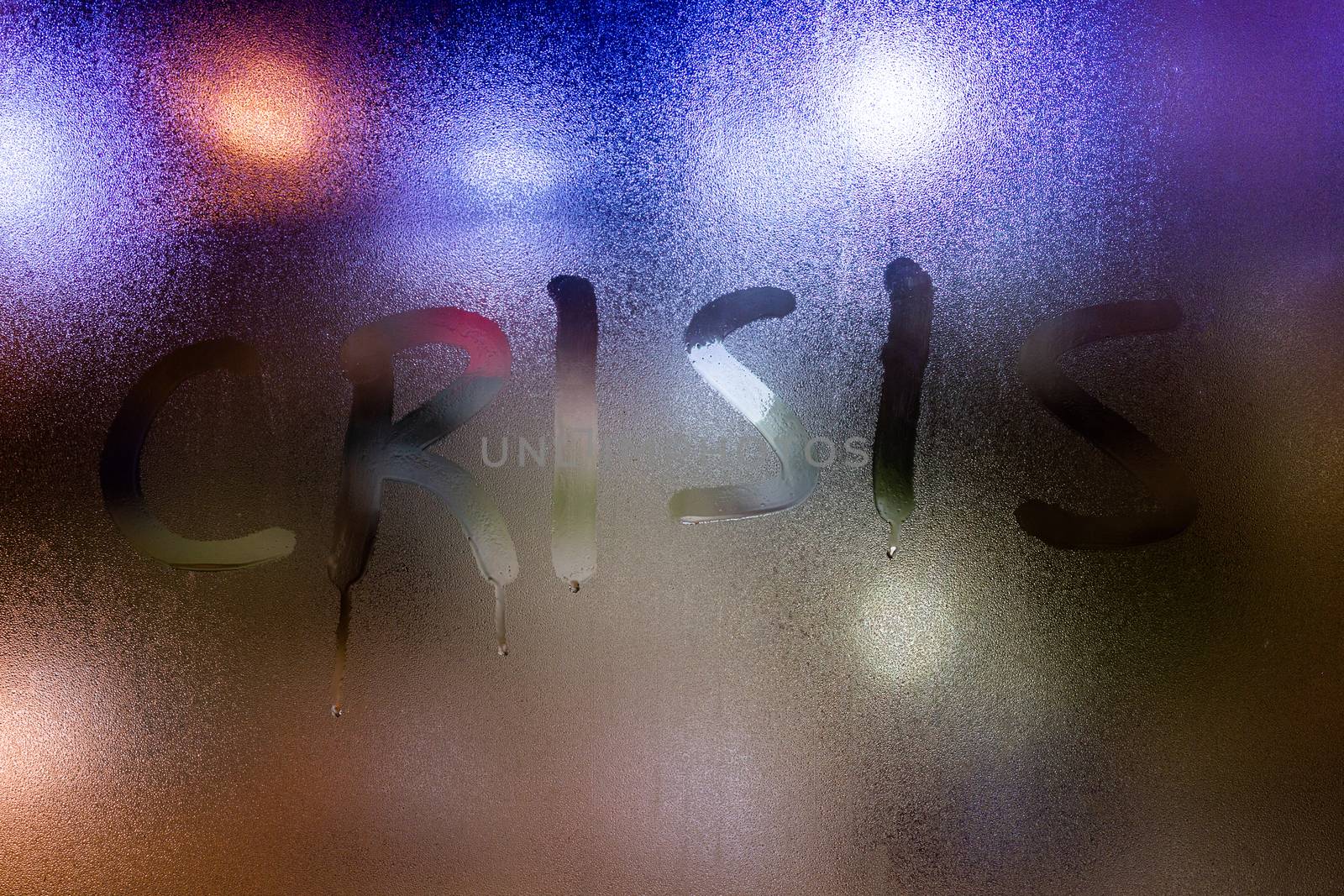 The word crisis written on night wet window glass close-up.