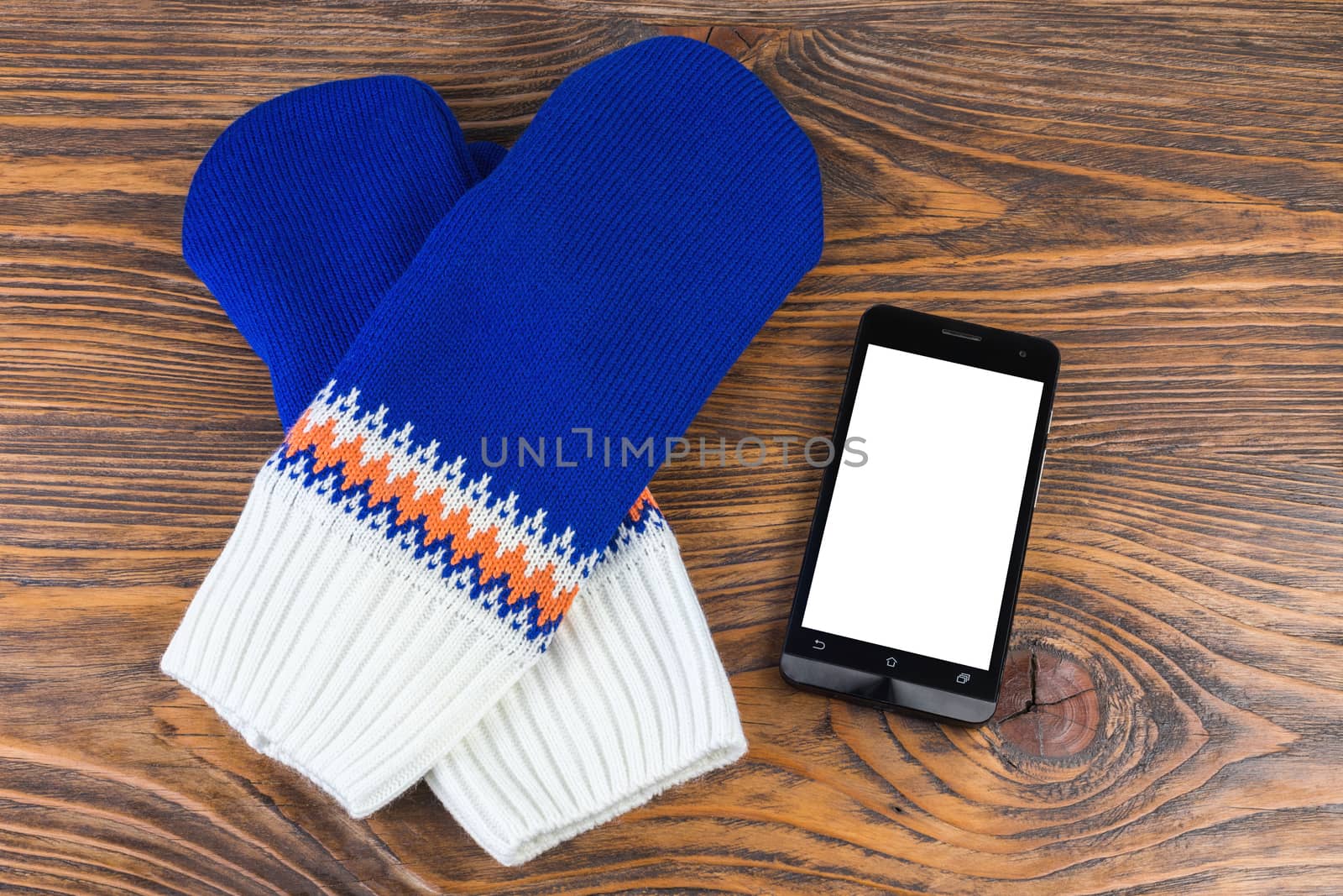 blue and white knited mittens with cellphone on wooden background.