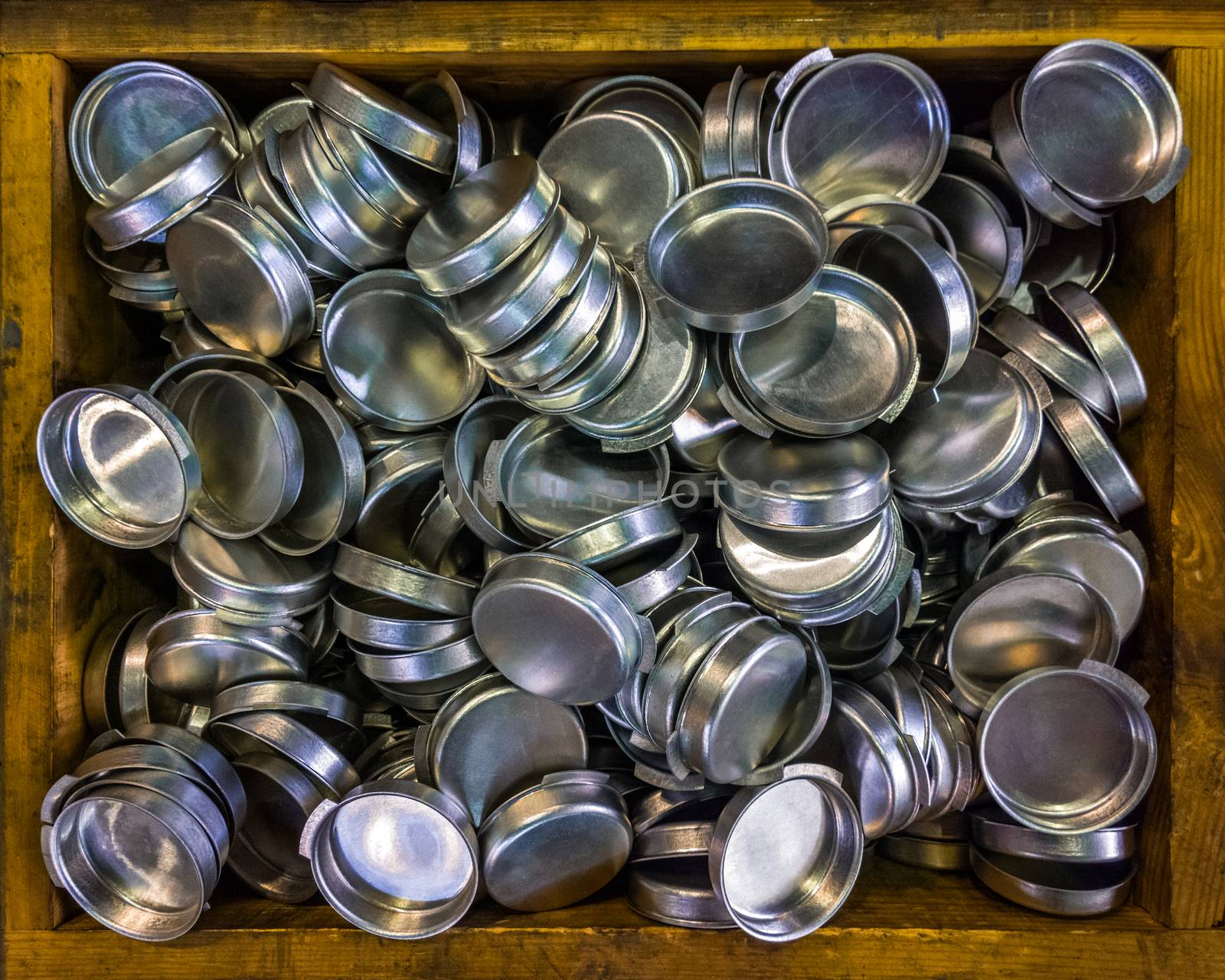 wooden box with batch od stamped shiny metal caps, selective focus top-down wiew.