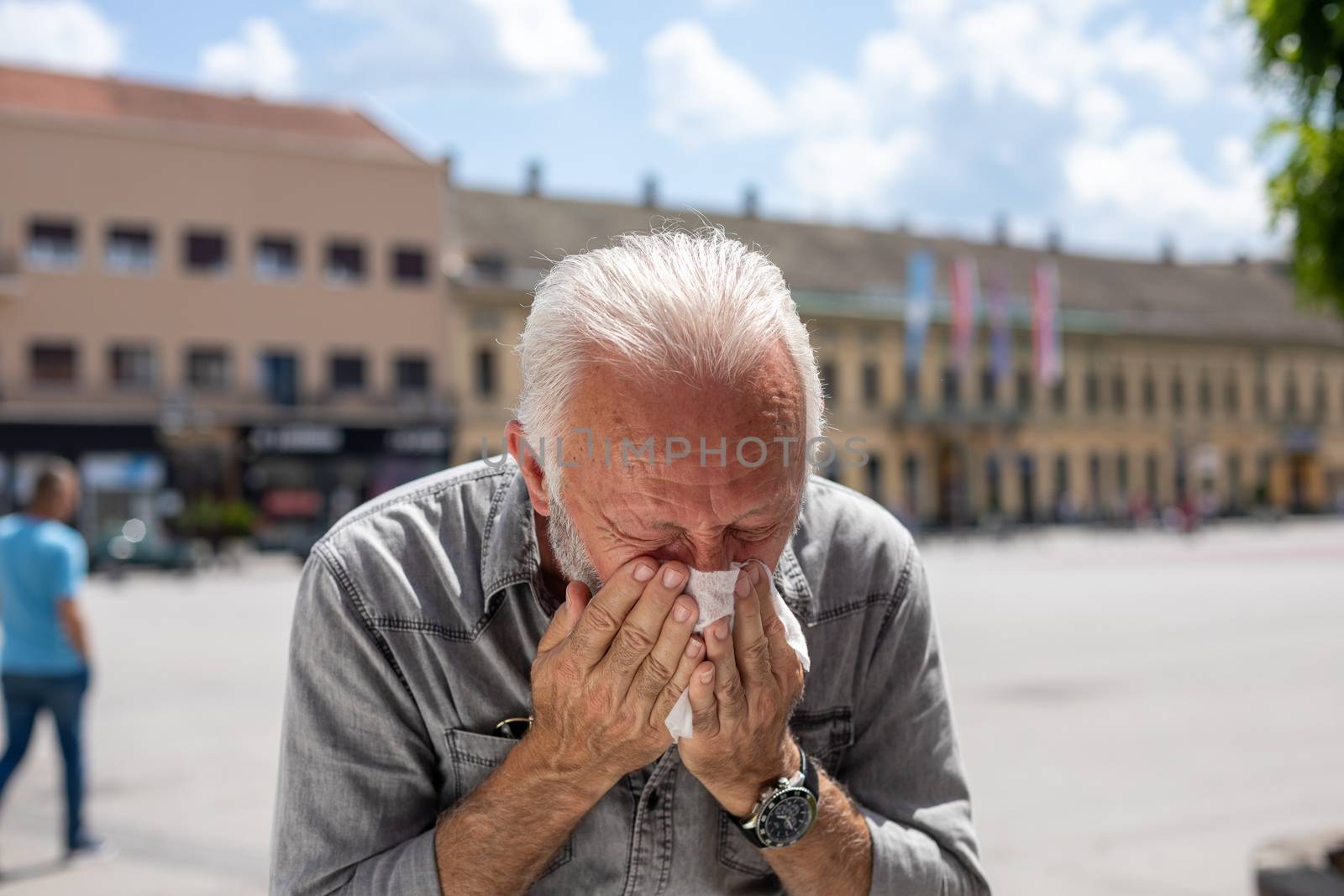 Old man man coughs and sneezes into a handkerchief on street, al by adamr