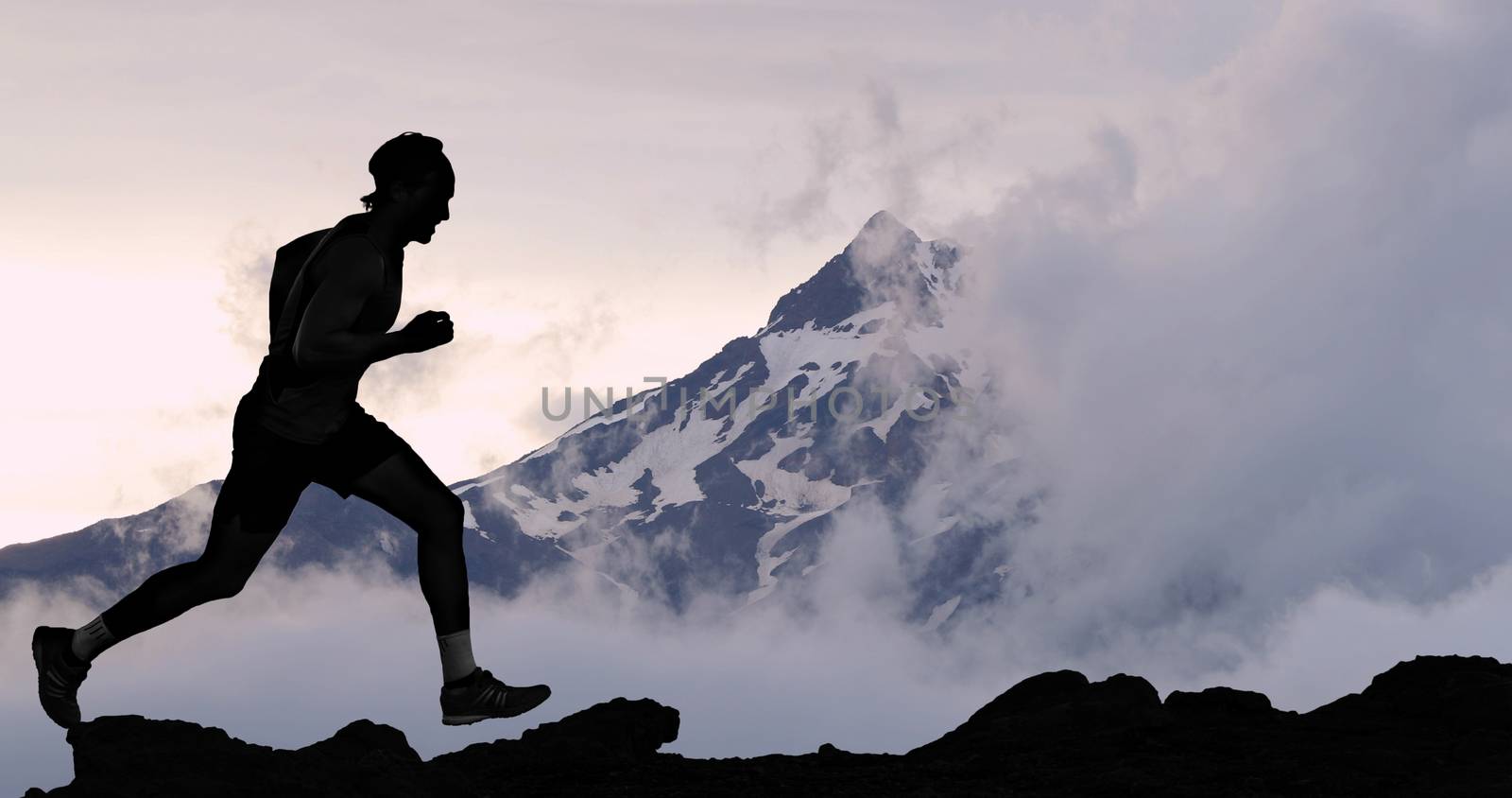 Running man athlete trail running in mountain summit background. Male runner on run training outdoors living active fit lifestyle. Silhouette at sunset.