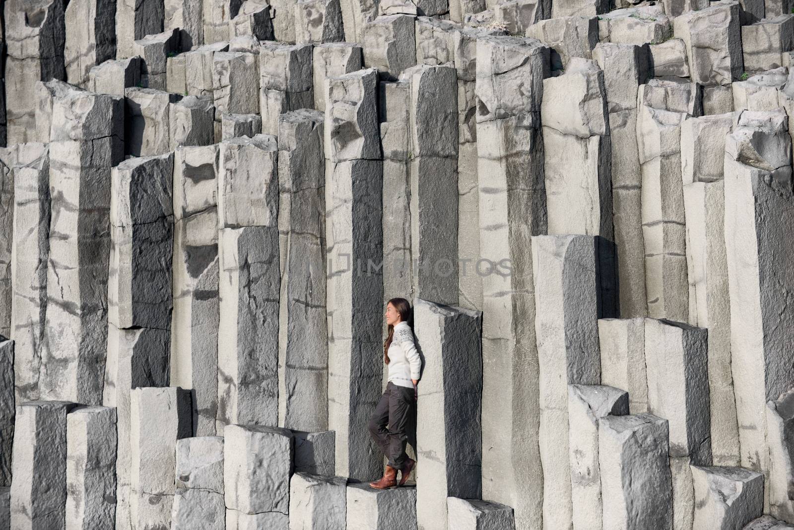 Iceland tourist at beach sitting on basalt columns on Reynisfjara beach, the black sand beach of Vik, South Iceland coast. Happy woman visiting tourist attraction destination.