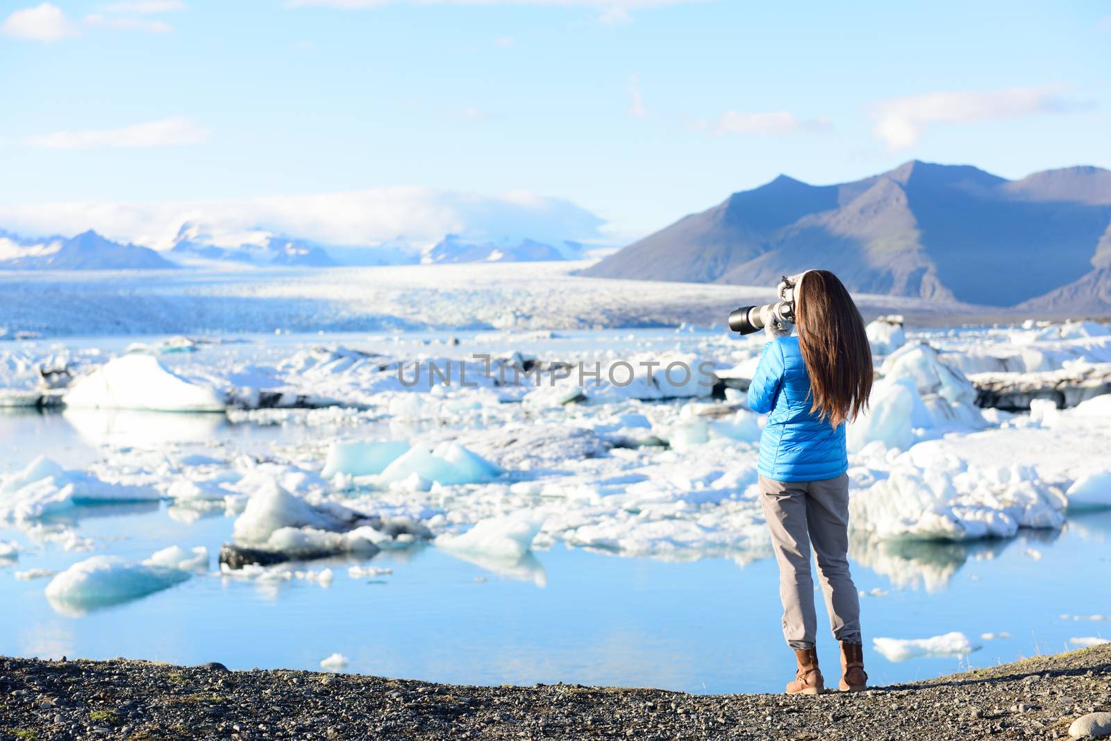 Photographer tourist woman taking photos with DSLR camera on travel on Iceland by Jokulsarlon glacial lagoon / glacier lake on Iceland. Happy tourist girl on travel in beautiful nature landscape by Maridav