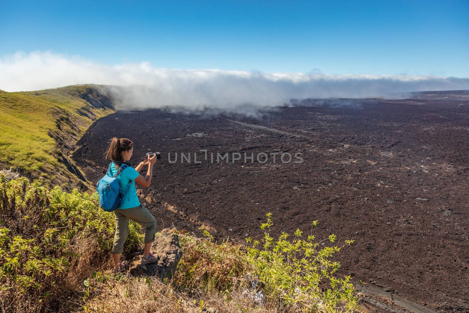 Galapagos tourist hiking on volcano Sierra Negra on Isabela Island taking photos with camera. Woman on hike on famous landmark, worlds 2nd largest active volcanic caldera, Galapagos Islands Ecuador.