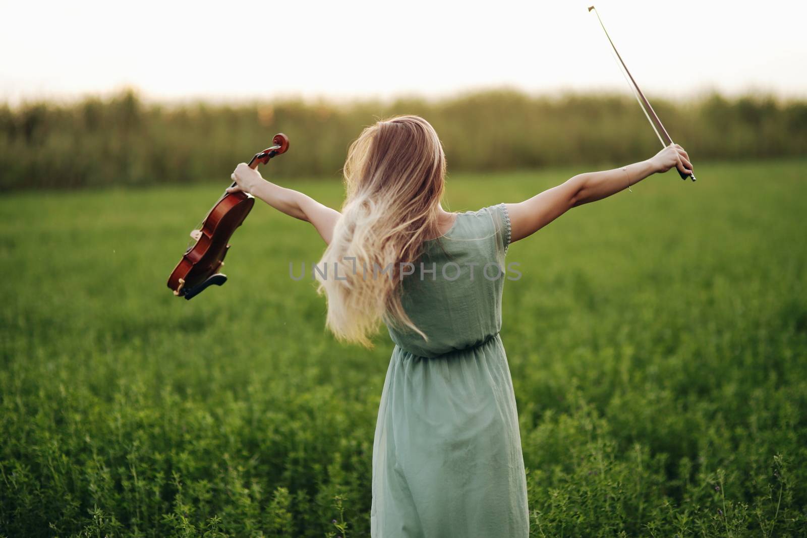 Happy musician violinist holding violin in her hands in sunset light by selinsmo