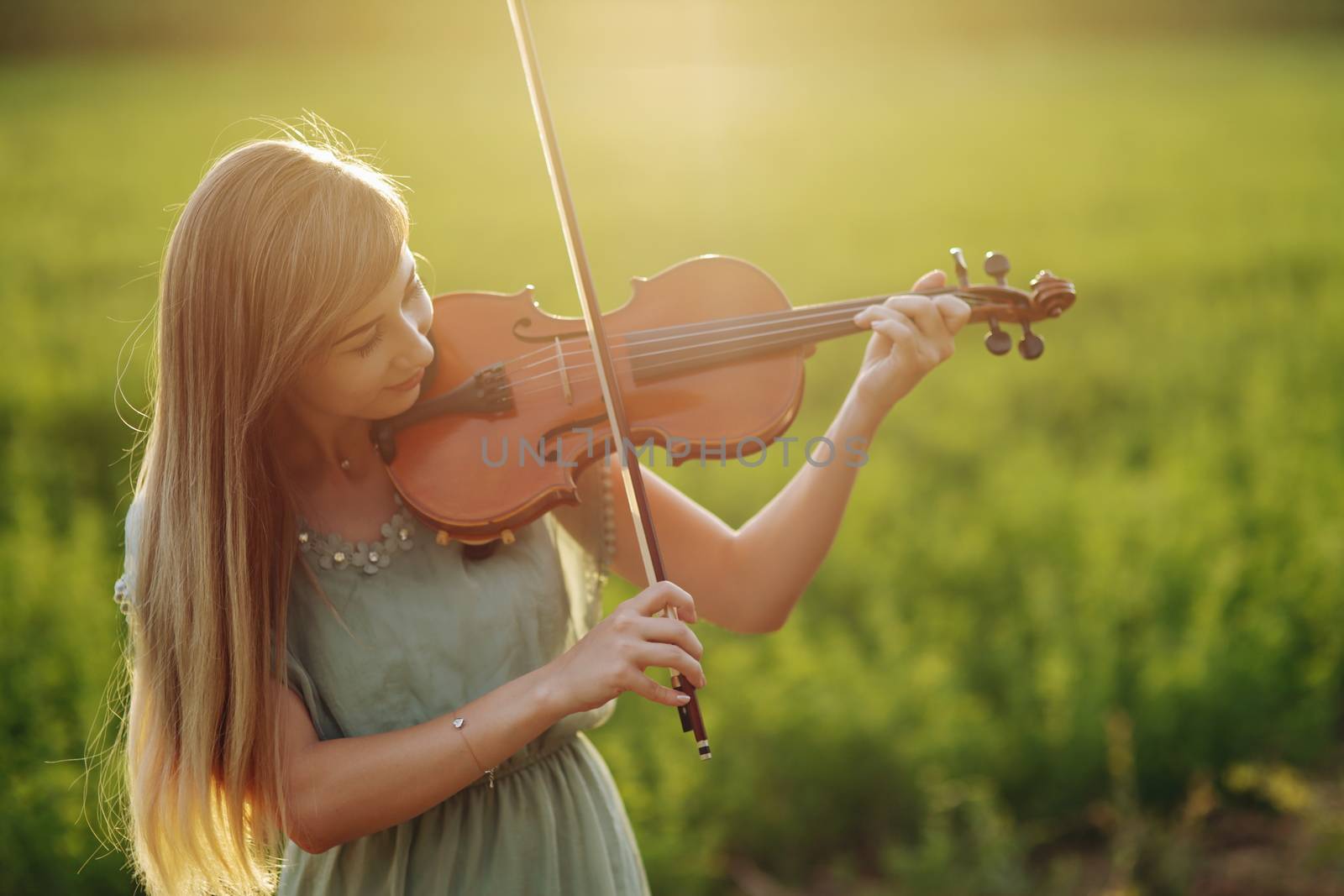 Romantic woman with loose hair playing the violin. Sunset light in nature. Violin training