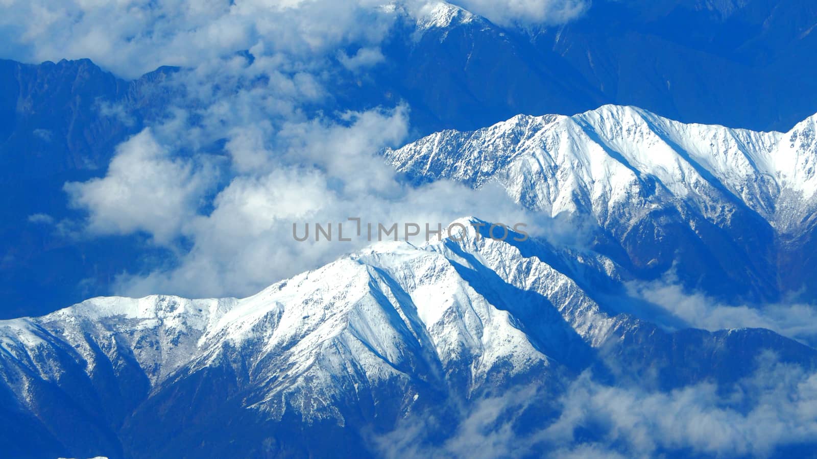 Top view angle images of snow hills around Fuji mountain and white light clouds and blue sky in Tokyo Japan which shoot from airlane.