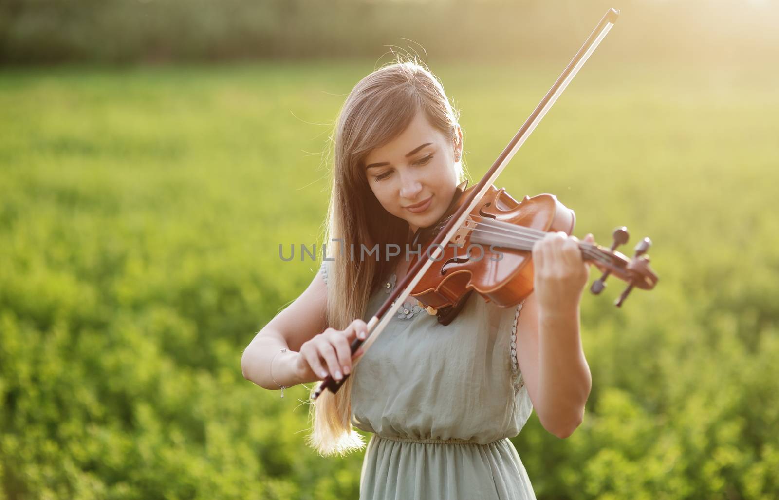 Romantic woman with loose hair playing the violin. Sunset light in nature. Violin training