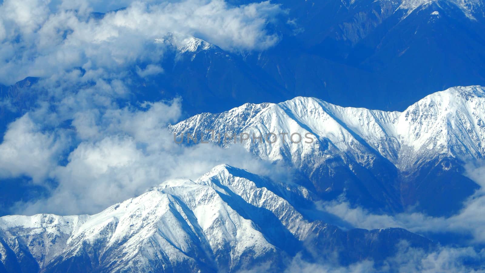 Top view angle images of snow hills around Fuji mountain and white light clouds and blue sky in Tokyo Japan which shoot from airlane.