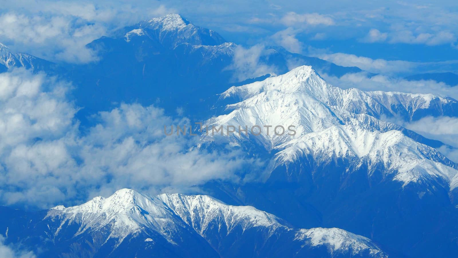 Top view angle images of snow hills around Fuji mountain and white light clouds and blue sky in Tokyo Japan which shoot from airlane.