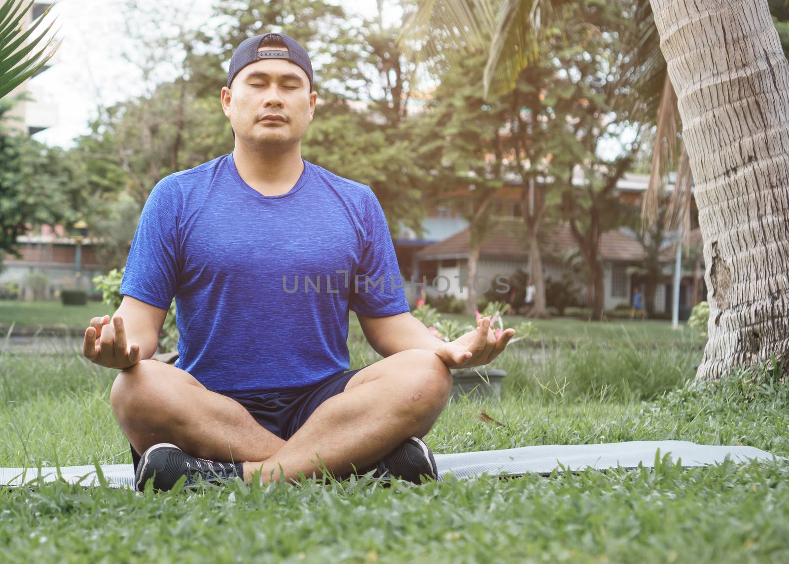 Sportsman meditate on the grass in the park. Young Asian men are healthy and fit to wear sportswear. Sit and relax with yoga  After exercise. fitness and sport  athletic body, balanced life, concept