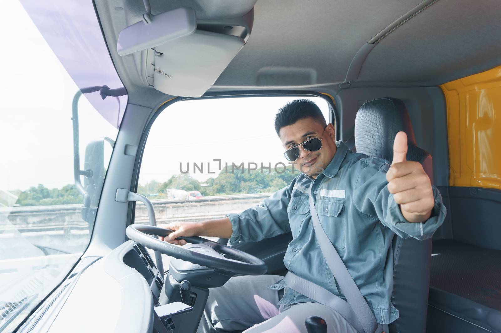 Professional truck driver, adult male Asian wearing sunglasses Smile and raise your hand. The young man worker is confident in the safety of the transport  and delivery business for a long time.