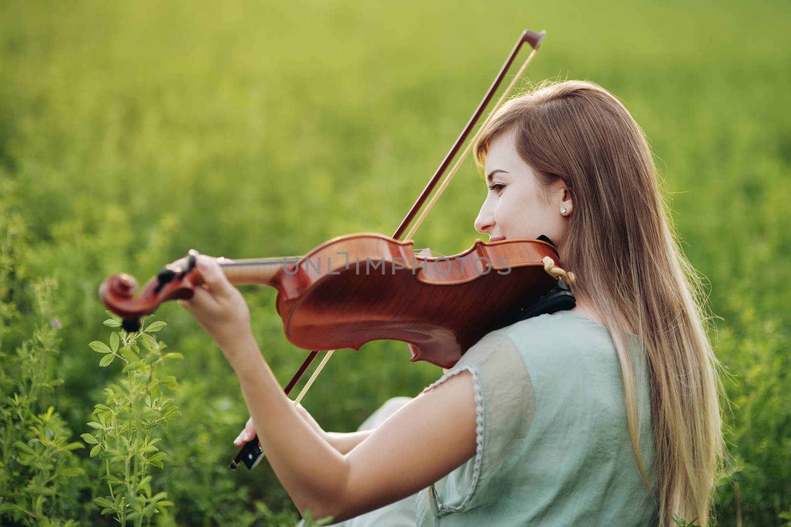 Romantic woman with loose hair playing the violin. Sunset light in nature. Violin training