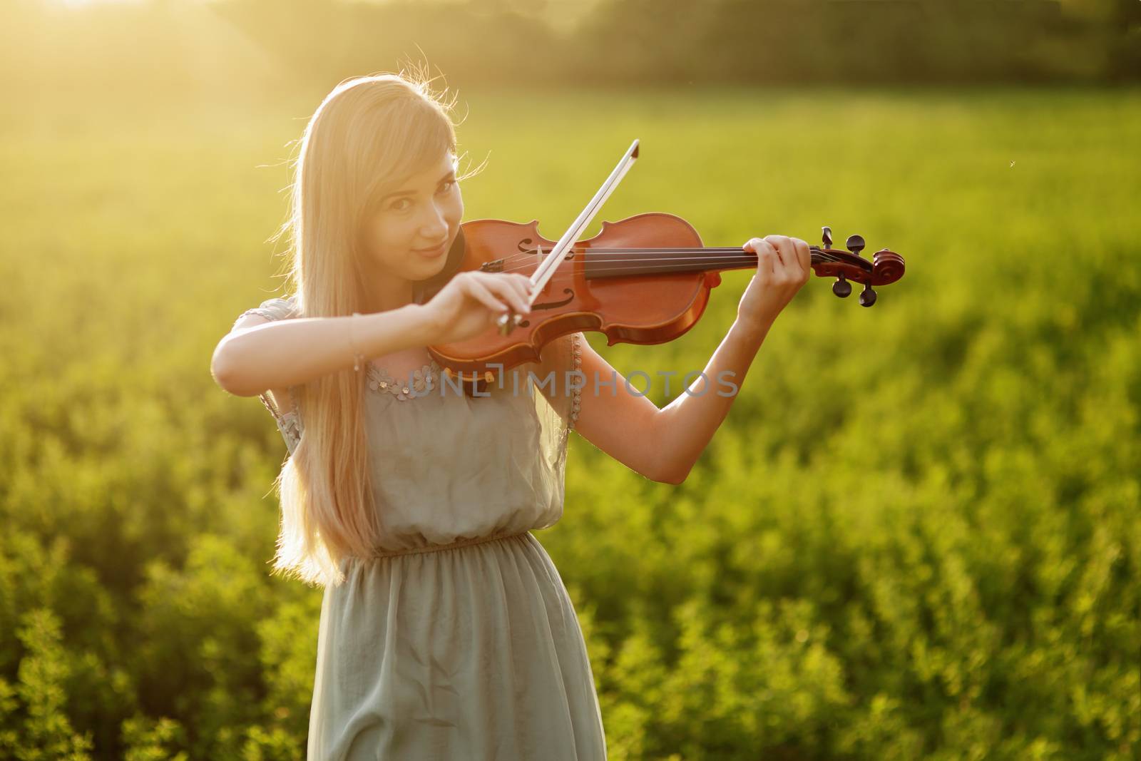 Romantic woman with loose hair playing the violin. Sunset light in nature. Violin training
