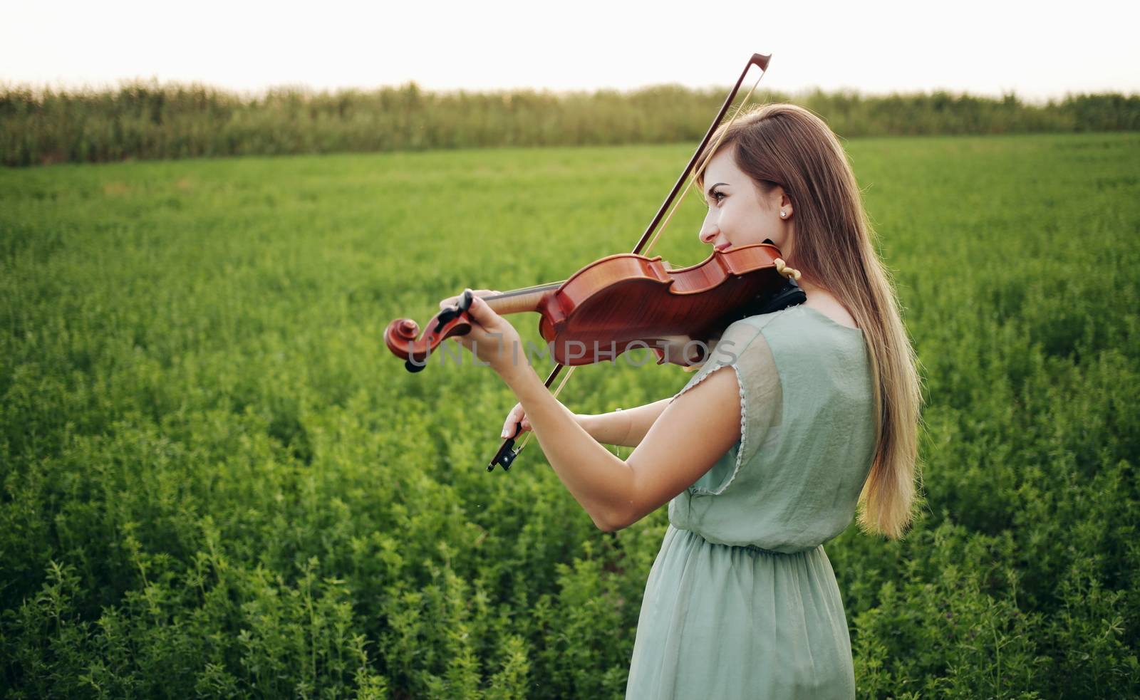 Romantic woman with loose hair playing the violin. Sunset light in nature. Violin training