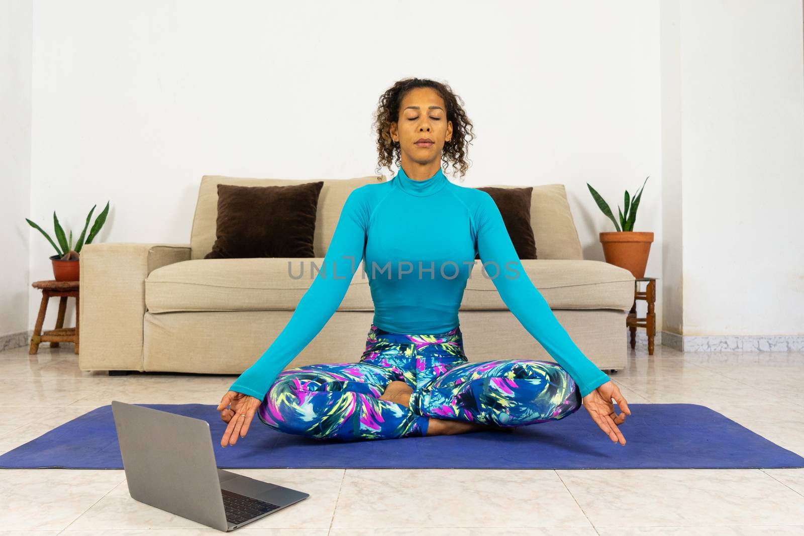 Brazilian black young woman training yoga at home with laptop in living room. Exercising on a mat.