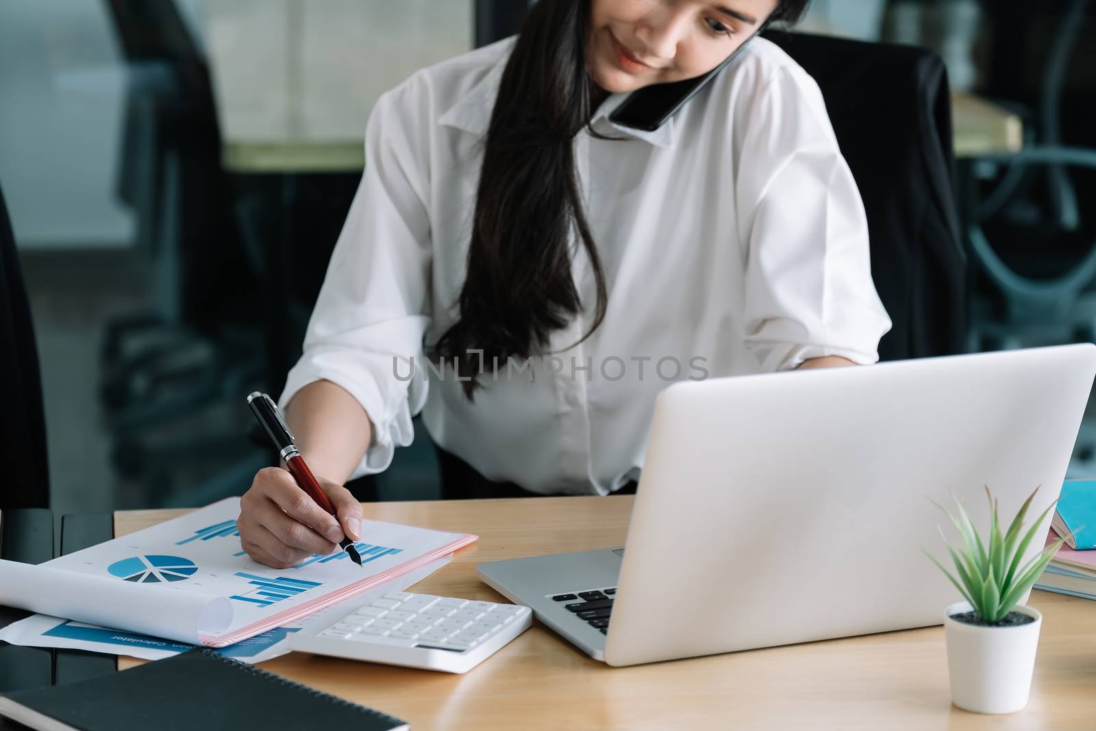 Young accountant hand holding smartphone to call marketing consultants and using laptop computer to analyze sales growth in the global workplace market. accounting concept.