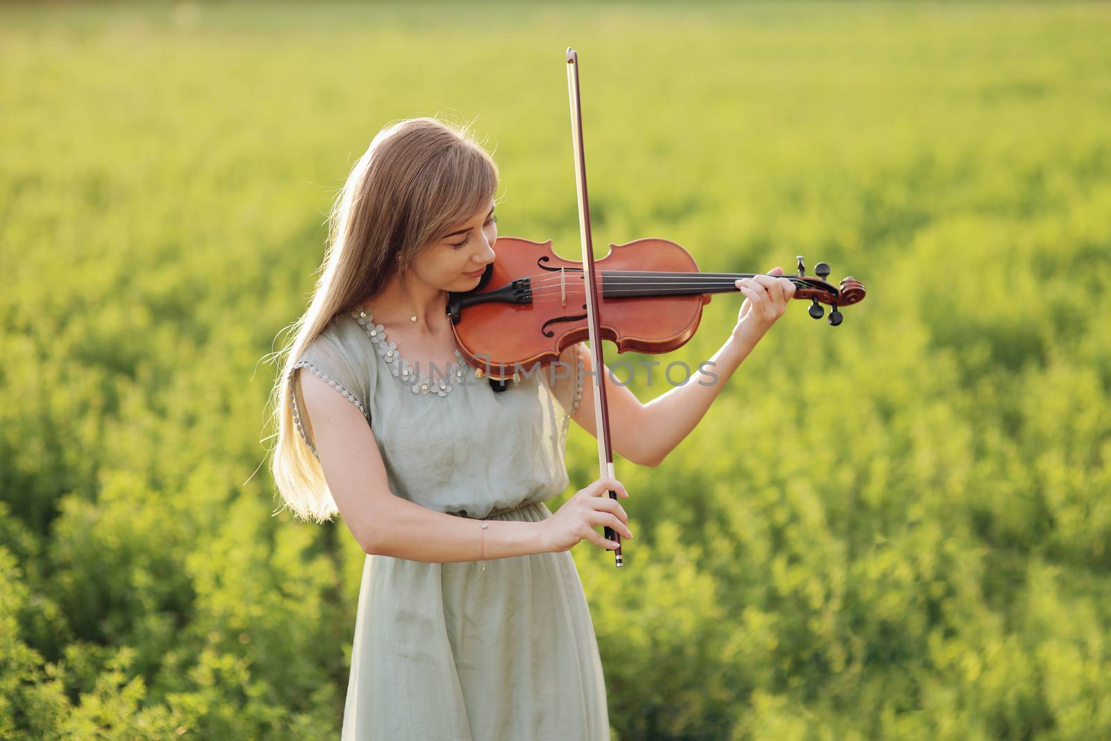 Romantic woman with loose hair playing the violin. Sunset light in nature by selinsmo