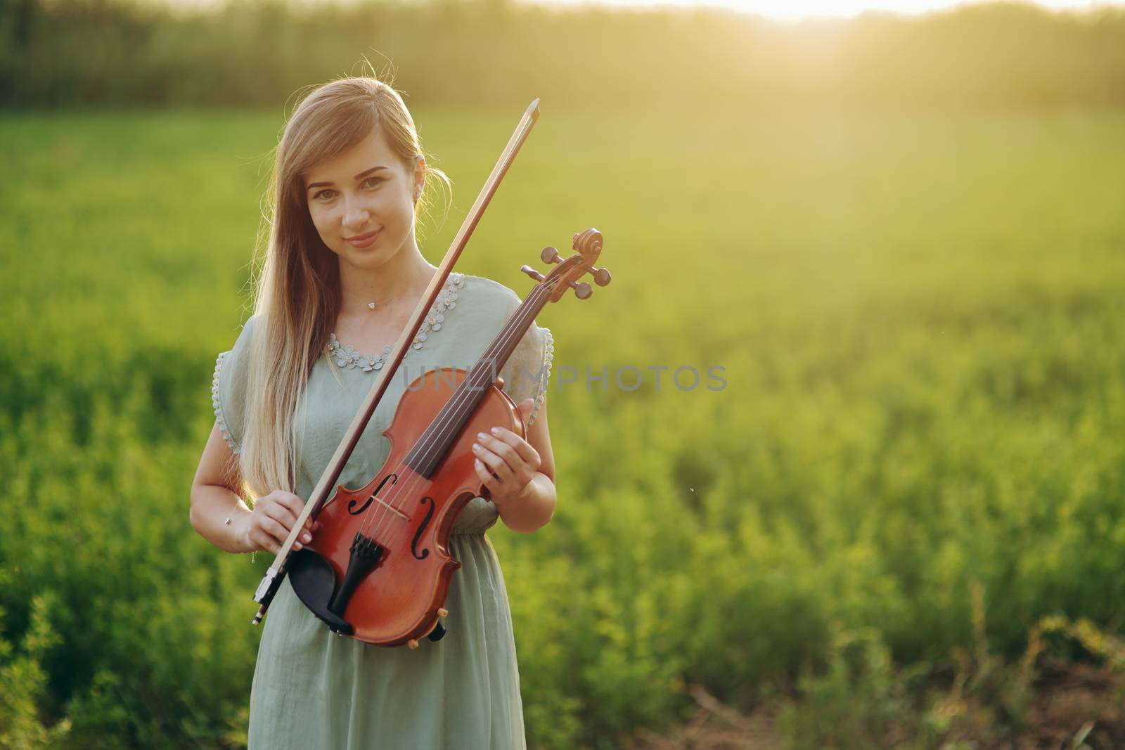 Female musician violinist holding a violin in her hands in sunset light by selinsmo