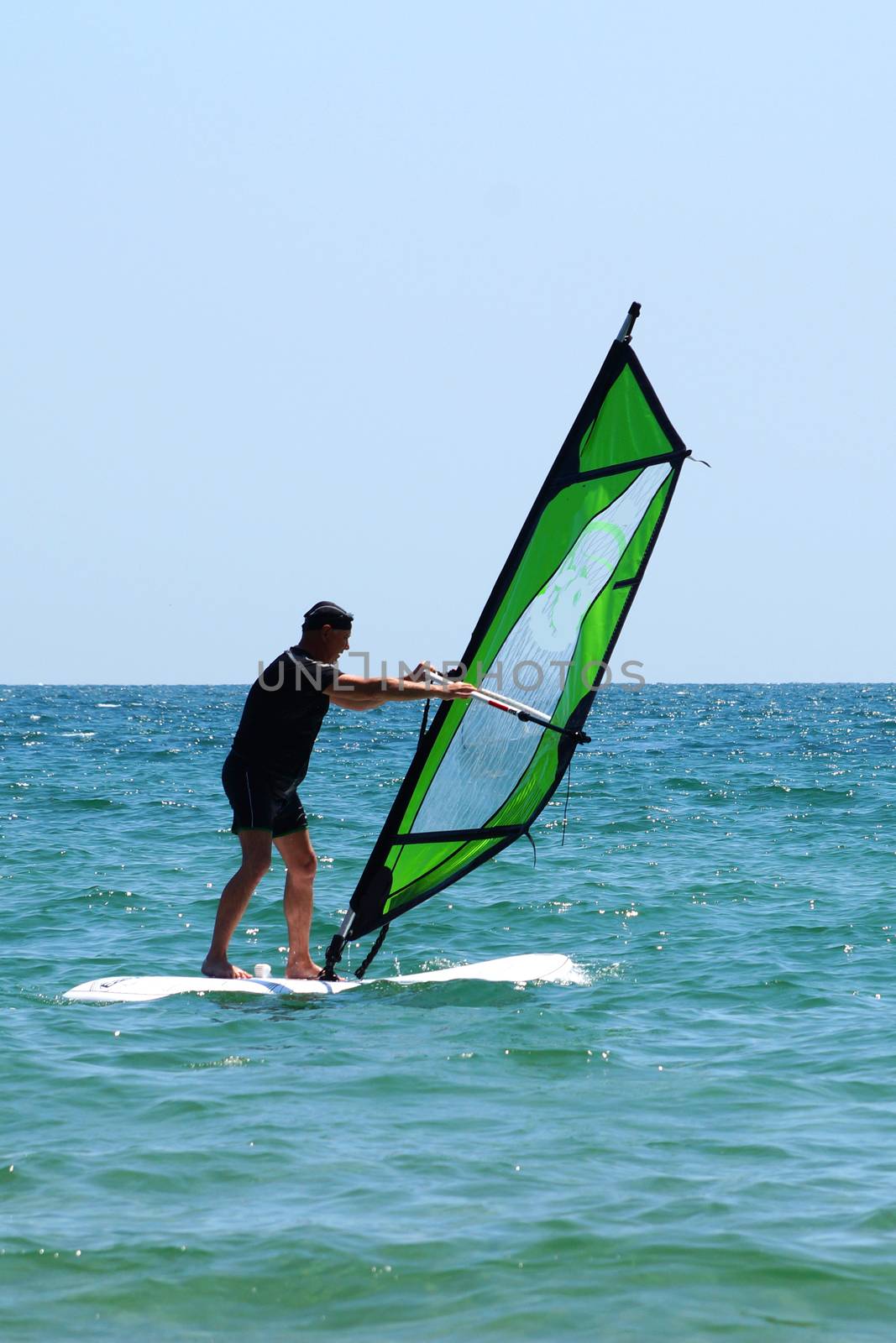 old man windsurfing in the sea on sunny day by Annado