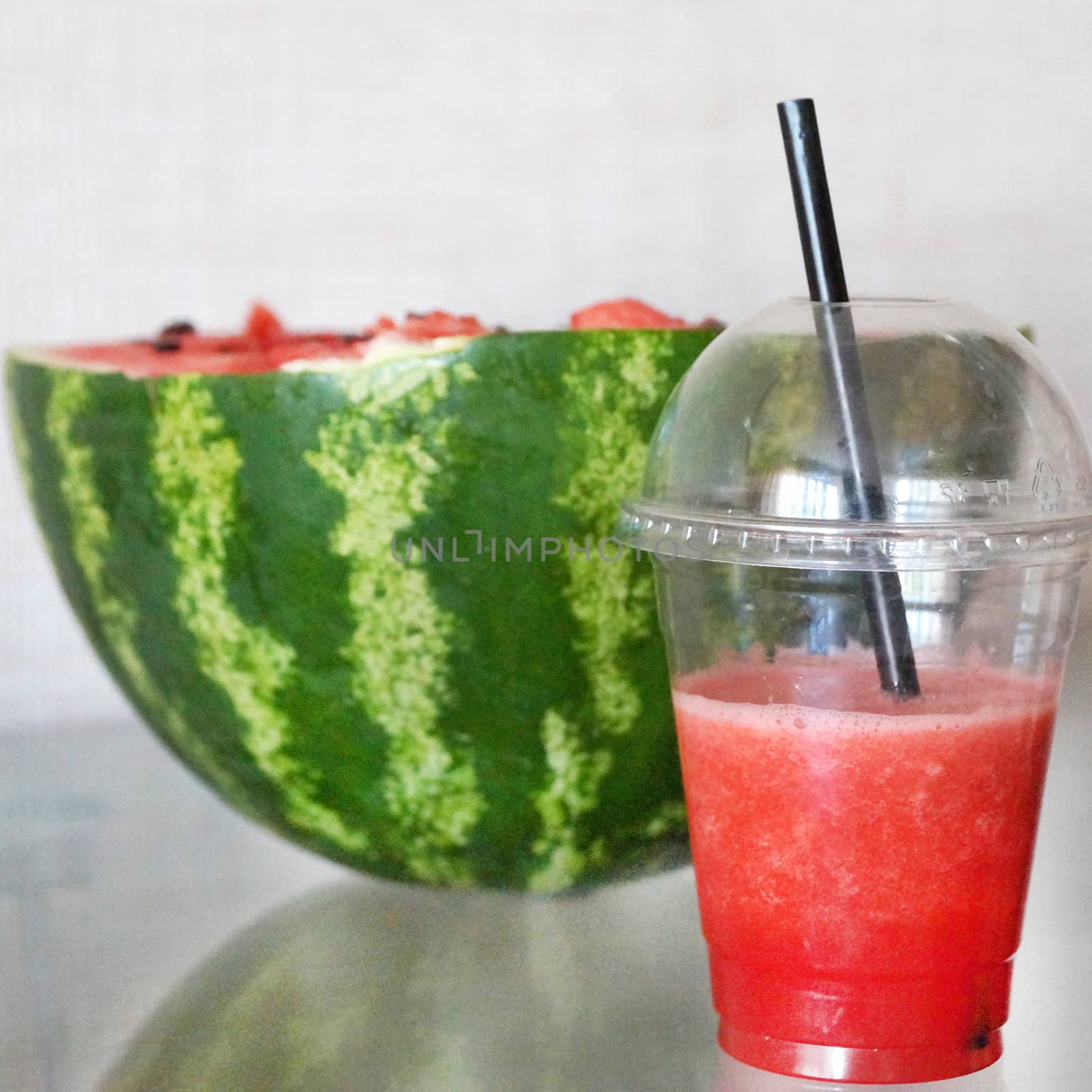 fresh watermelon in a glass with a straw and half a watermelon by Annado