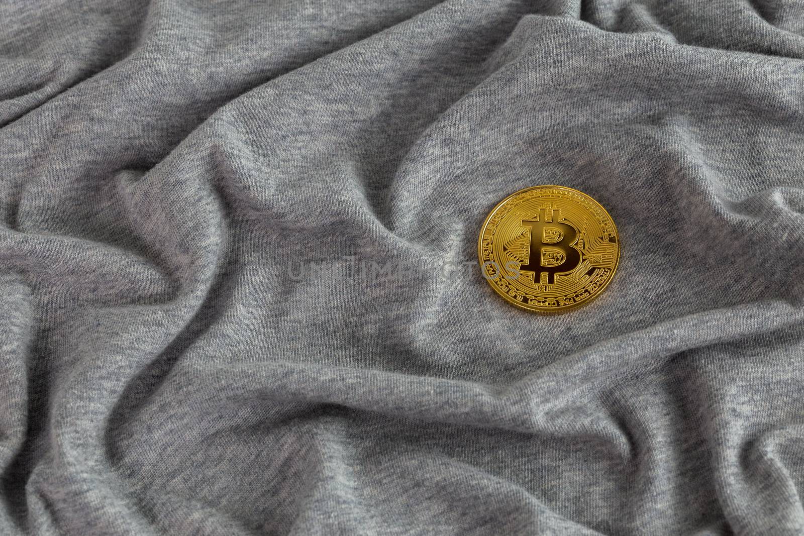 Golden bitcoin shiner on gray crumpled cotton cloth.
