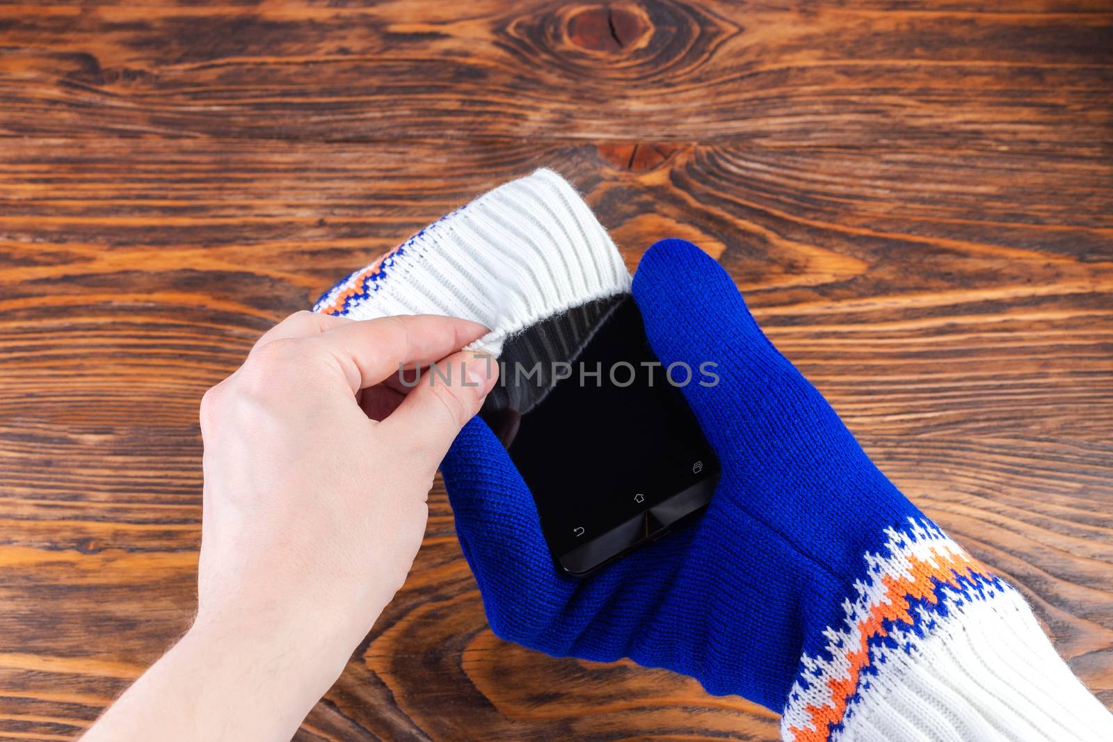 hand putting a cellphone into white-blue mittens.