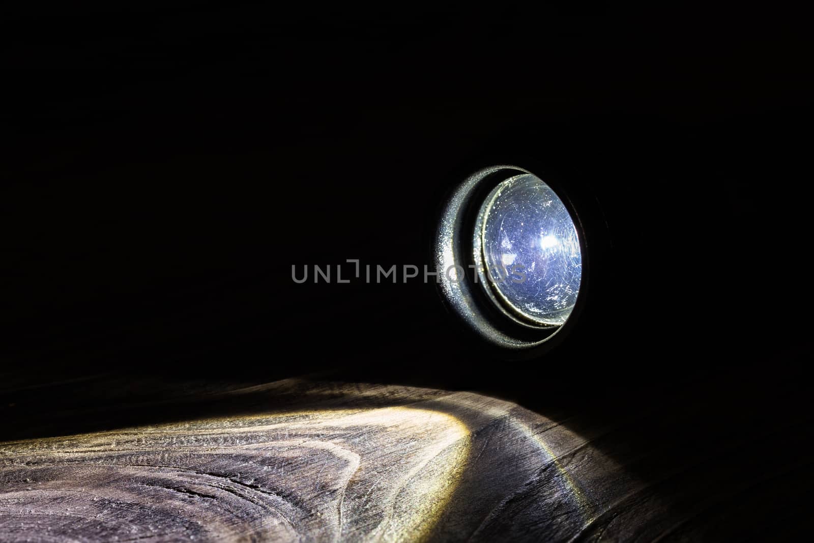 Black led operational flashlight on rough wooden surface - closeup with selective focus. Nighttime covert activity or search background.